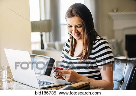 Stock Photography - Hispanic woman using laptop and cell phone. Fotosearch
