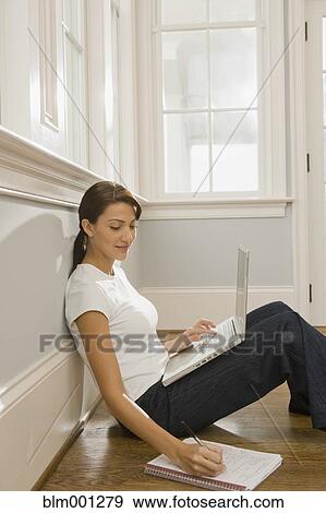 Stock Photo - Hispanic woman using laptop and making notes. Fotosearch