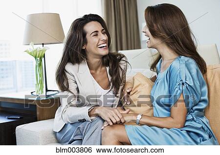 Stock Photograph - Hispanic women laughing on sofa. Fotosearch