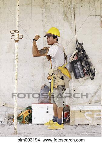 Hispanic worker flexing biceps on construction site View Large Photo Image Picture - Hispanic worker flexing biceps on construction site. Fotosearch