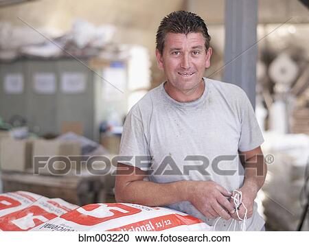 Stock Image - Hispanic worker holding bag in factory warehouse. Fotosearch