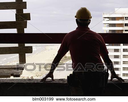 Stock Photo - Hispanic worker looking down from construction site. Fotosearch