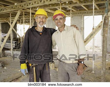 Picture - Hispanic workers hugging at construction site. Fotosearch