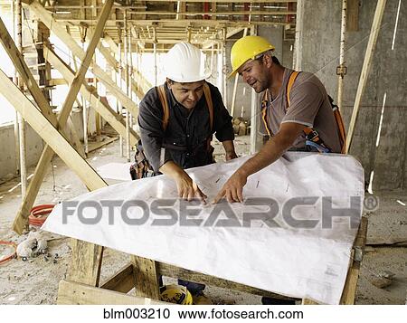 Stock Image - Hispanic workers looking at blueprints on construction site. Fotosearch