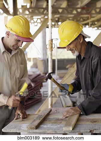 Stock Photo - Hispanic workers using hammers at construction site. Fotosearch