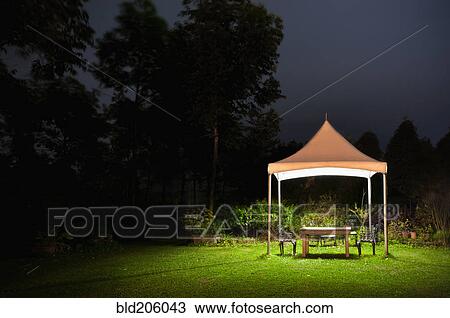 Stock Image - Illuminated canopy and table in garden. Fotosearch