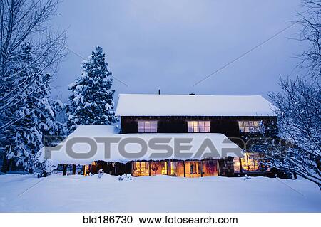 Stock Image - Illuminated house in snowy field at dusk. Fotosearch