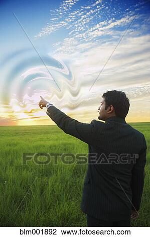 Stock Image - Indian businessman swirling sky with finger. Fotosearch