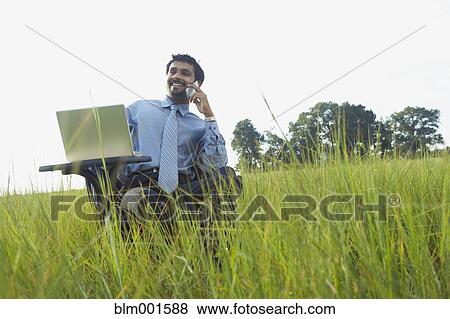 Indian businessman talking on cell phone in field View Large Photo Image Stock Photo - Indian businessman talking on cell phone in field. Fotosearch