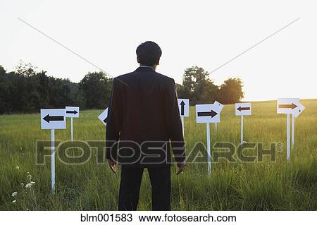Stock Image - Indian businessman with arrow signs in field. Fotosearch