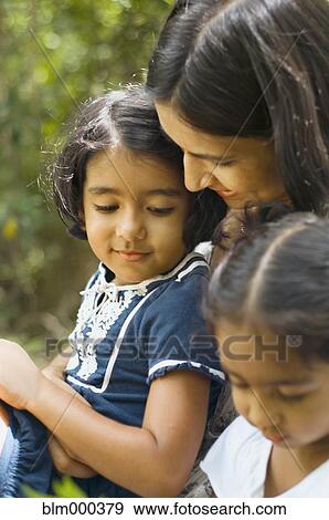 Stock Photo - Indian mother sitting with daughters outdoors. Fotosearch