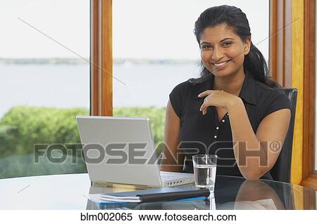 Stock Photography - Indian woman at table with laptop. Fotosearch