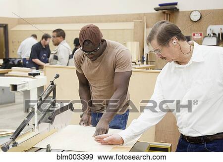 Stock Photo - Instructor giving explanation to man in workshop. Fotosearch