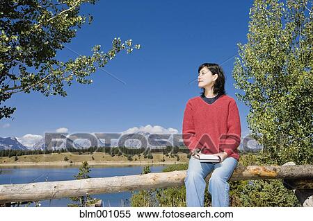 Stock Photography - Japanese woman sitting on fence with mountains in background. Fotosearch