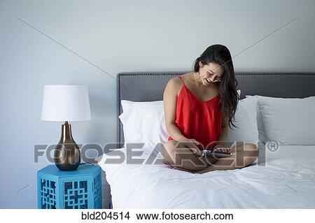 Picture - Japanese woman using tablet computer on bed. Fotosearch