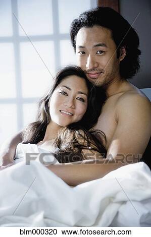 Stock Image - Korean couple hugging in bed. Fotosearch