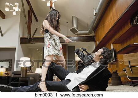 Stock Image - Korean man filming woman in living room. Fotosearch