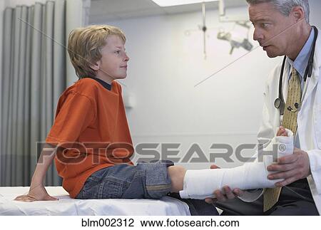 Stock Image - Male doctor examining boy with cast. Fotosearch