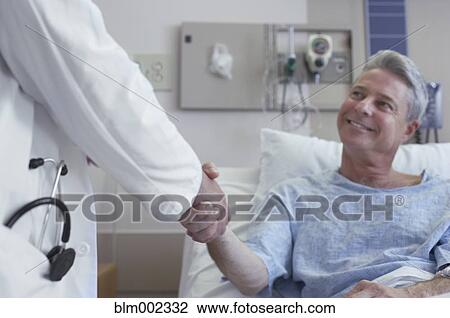 Stock Image - Male doctor shaking hands with patient. Fotosearch