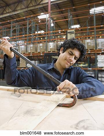 Stock Photo - Male warehouse worker opening box with crowbar. Fotosearch