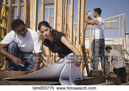Stock Photography - Man and woman reviewing blueprints at construction site. Fotosearch
