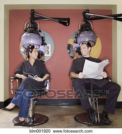 Stock Image - Man and woman under hair dryers in salon. Fotosearch