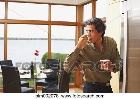 Stock Photo - Man eating ice cream next to refrigerator. Fotosearch