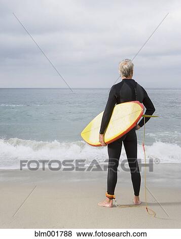 Stock Photo - Man holding surfboard at beach. Fotosearch