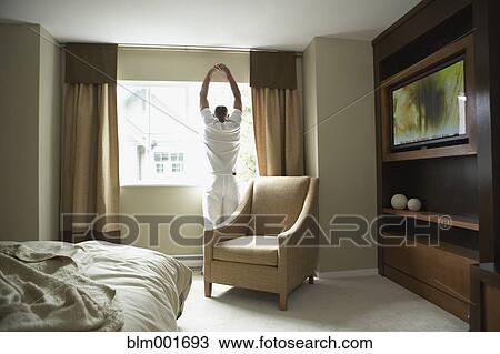 Stock Image - Man stretching and looking out window. Fotosearch