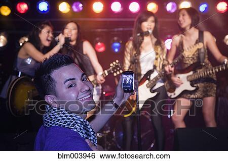 Stock Photograph - Man video recording musical group onstage. Fotosearch