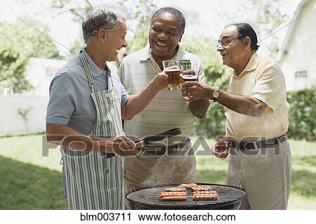 Stock Image - Men toasting beers over backyard barbecue grill. Fotosearch