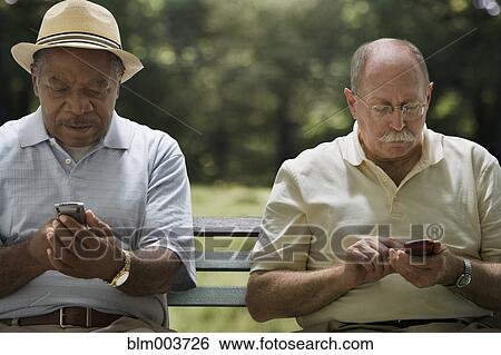 Stock Photograph - Men using cell phones on park bench. Fotosearch