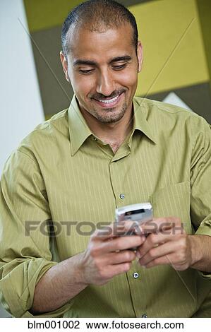 Stock Image - Middle Eastern man text messaging on cell phone. Fotosearch