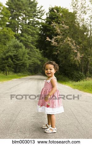 Stock Image - Mixed race baby girl standing on remote roadway. Fotosearch