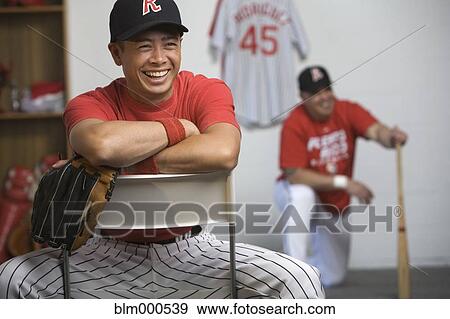 Stock Photo - Mixed race baseball player laughing in locker room. Fotosearch
