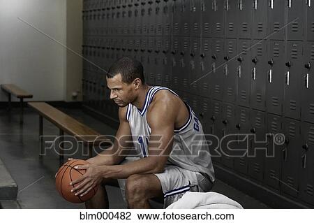 Stock Image - Mixed race basketball player sitting in locker room. Fotosearch