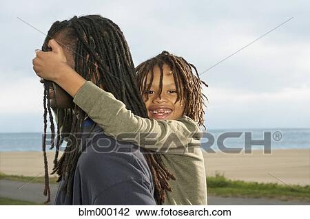 Stock Image - Mixed Race boy covering father’s eyes. Fotosearch