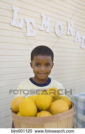 Stock Image - Mixed race boy holding basket of lemons. Fotosearch