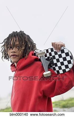 Stock Image - Mixed Race boy holding skateboard. Fotosearch