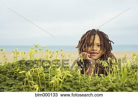 Stock Image - Mixed Race boy laying in plants. Fotosearch