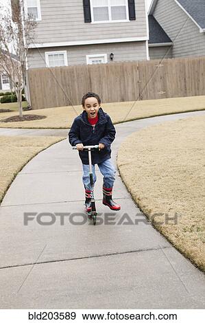 Stock Photo - Mixed race boy playing on scooter on suburban street. Fotosearch