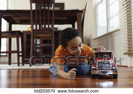 Stock Photo - Mixed race boy playing with fire truck on floor. Fotosearch