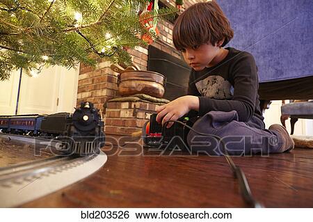 Stock Photograph - Mixed race boy playing with train under Christmas tree. Fotosearch