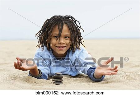 Stock Image - Mixed Race boy stacking stones on sand. Fotosearch