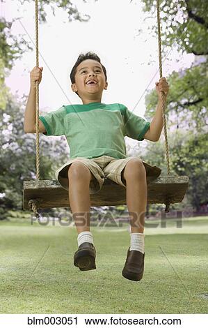 Stock Image - Mixed race boy swinging in backyard. Fotosearch