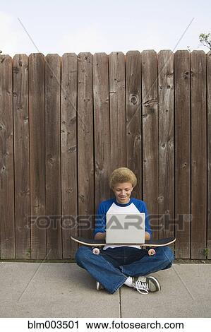 Stock Image - Mixed race boy typing on laptop outdoors. Fotosearch