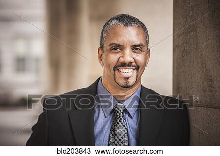 Stock Image - Mixed race businessman leaning on column. Fotosearch