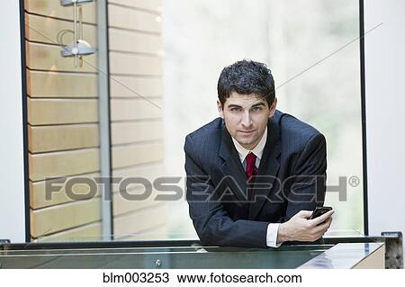 Stock Image - Mixed race businessman leaning on office railing. Fotosearch
