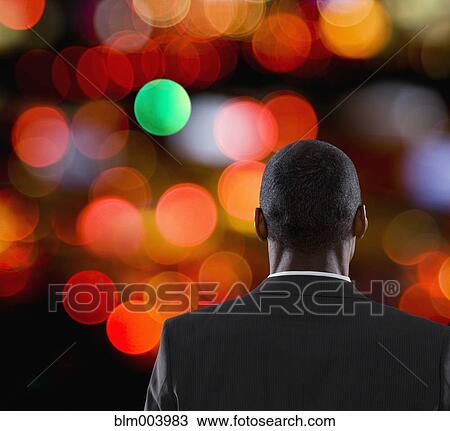 Stock Image - Mixed race businessman looking at blurred city lights. Fotosearch