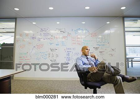 Stock Image - Mixed race businessman sitting in front of whiteboard. Fotosearch